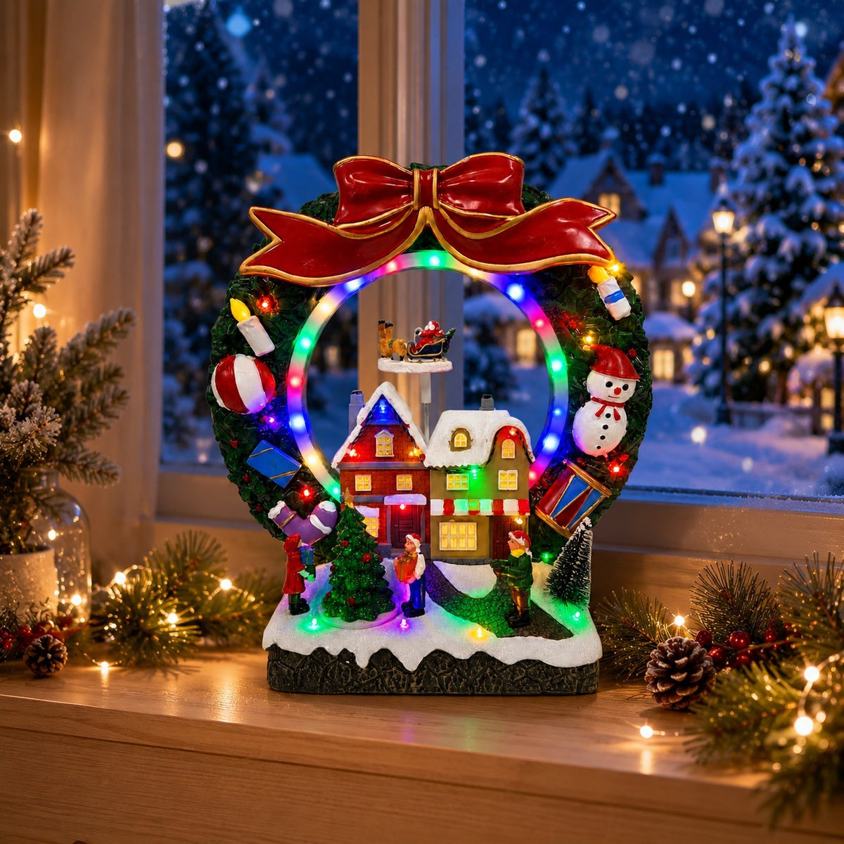 Lighted Christmas wreath village scene on a windowsill with Santa sleigh and snowy houses