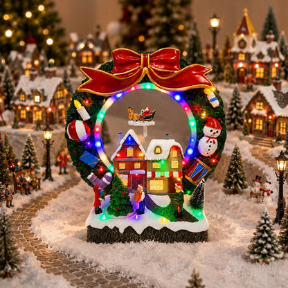 Lighted Christmas wreath village scene on a windowsill with Santa sleigh and snowy houses